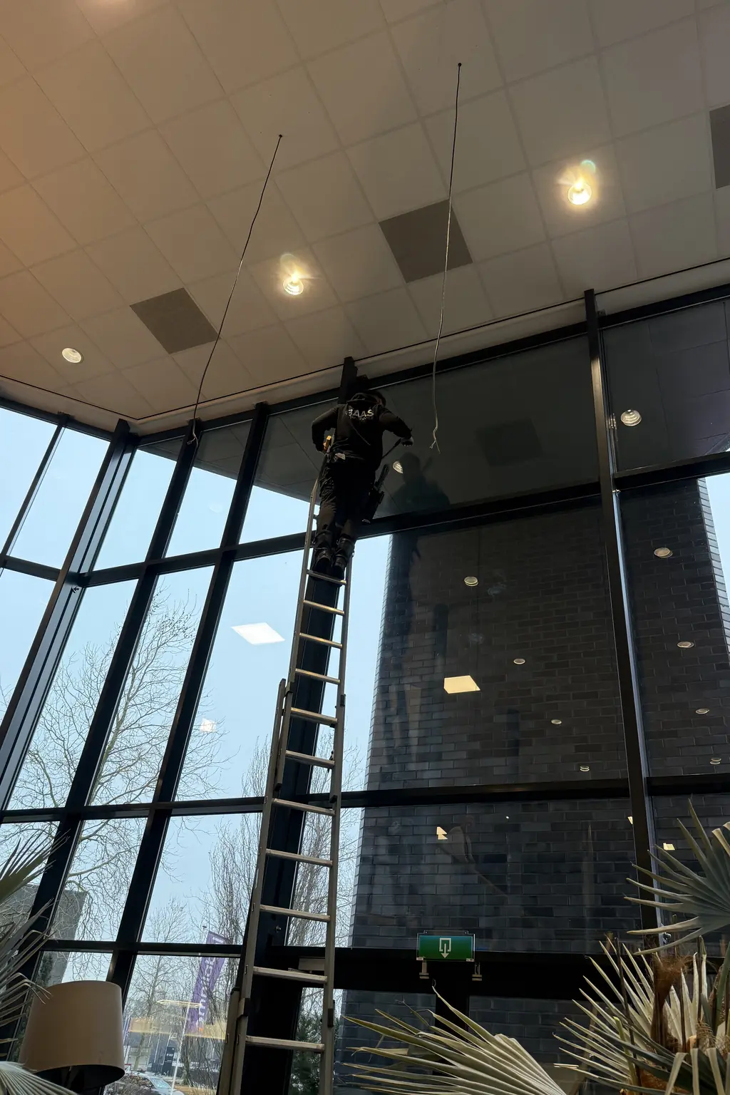 Medewerker van Baas Totaalservice wast een hoge glazen pui vanaf een ladder
